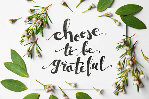 chose to be grateful in black cursive writing with a white background and green leaves and flowers surrounding it