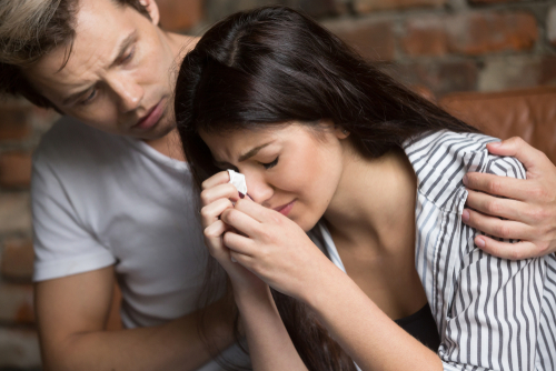 Woman crying into a tissue while a man comforts her.