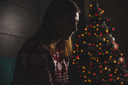 Loney woman looking sad sitting next to a lit christmas tree