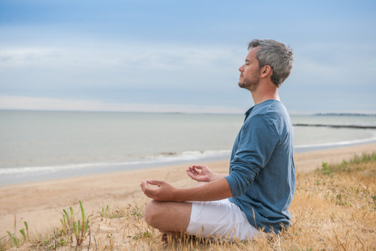 Middle age man meditating in the grass near a beach