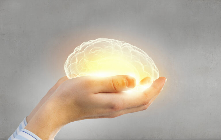 Two male hands carefully holding a brain that is illuminated in light.