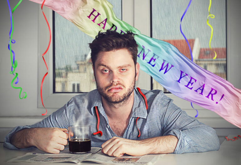 Disheveled and miserable man with a cup of coffee and a Happy New Year banner in the back