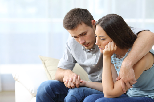 Young man and woman sitting on couch comforting each other