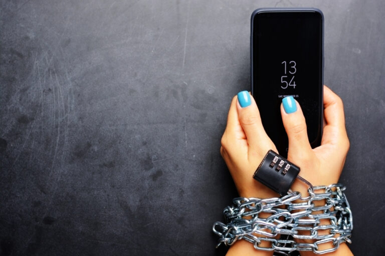 Woman's hands with blue finger nail polish, holding a cell phone with chains around her wrists.