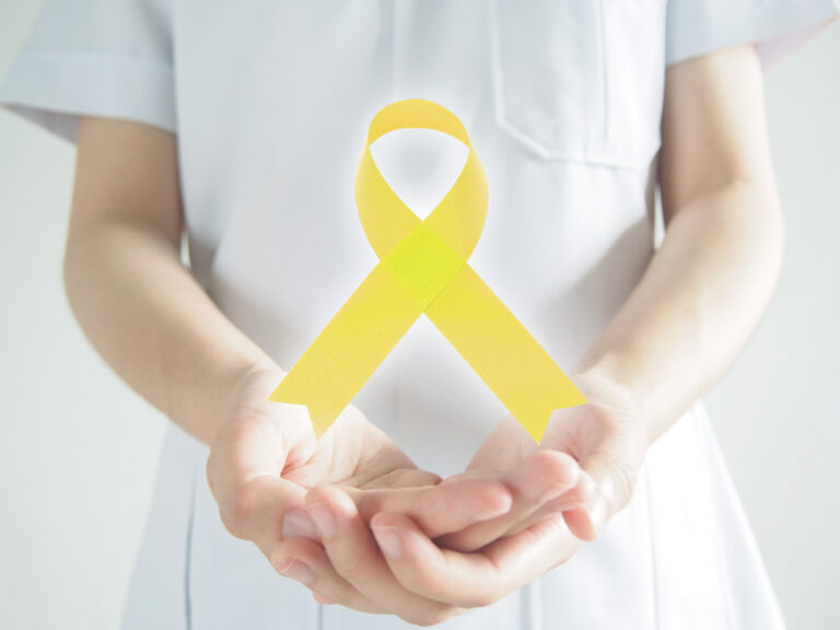 Woman in white nurses uniform, holding a yellow awareness ribbon for suicide prevention month.
