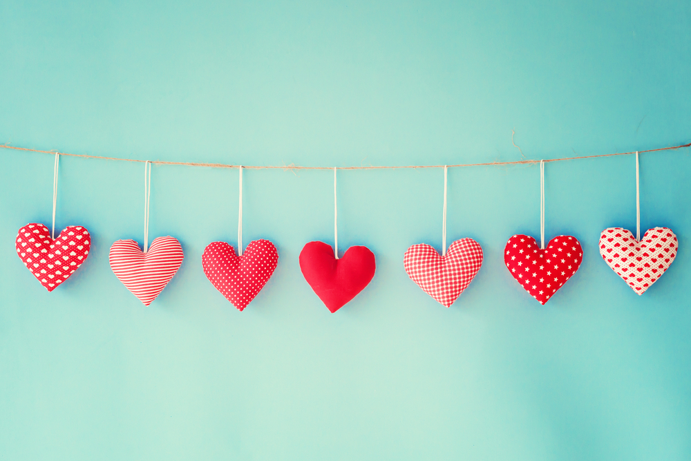 Small red Valentine's Day hearts, hanging on a string, with a teal background