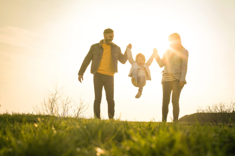Two parents swing a happy child between their arms at sunset