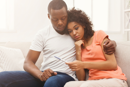 Sad African American Couple Sitting On A Couch Indoors Looking At A Pregnancy Test